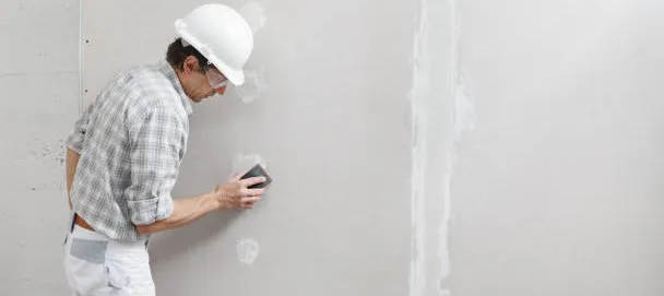 Persona alisando pared de yeso con herramienta de acabado en obra
